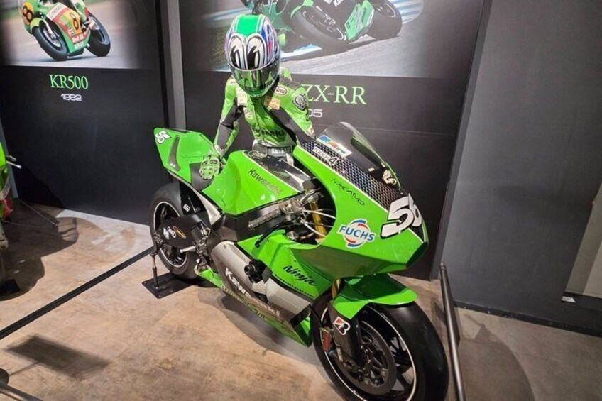 A green motorcycle with racing numbers and a helmet, displayed in a showroom. 3