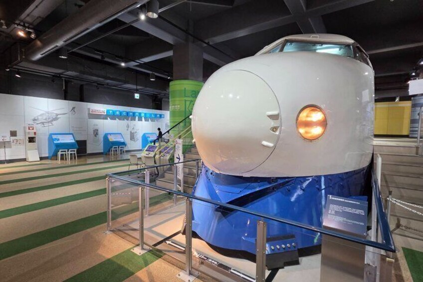 A space shuttle on display with a blue protective cover, a glass barrier, and informational panels in the background. 1