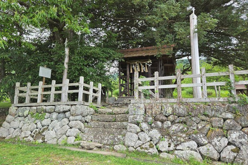 A stone wall, wooden fence, and a small shrine with a bell. 5