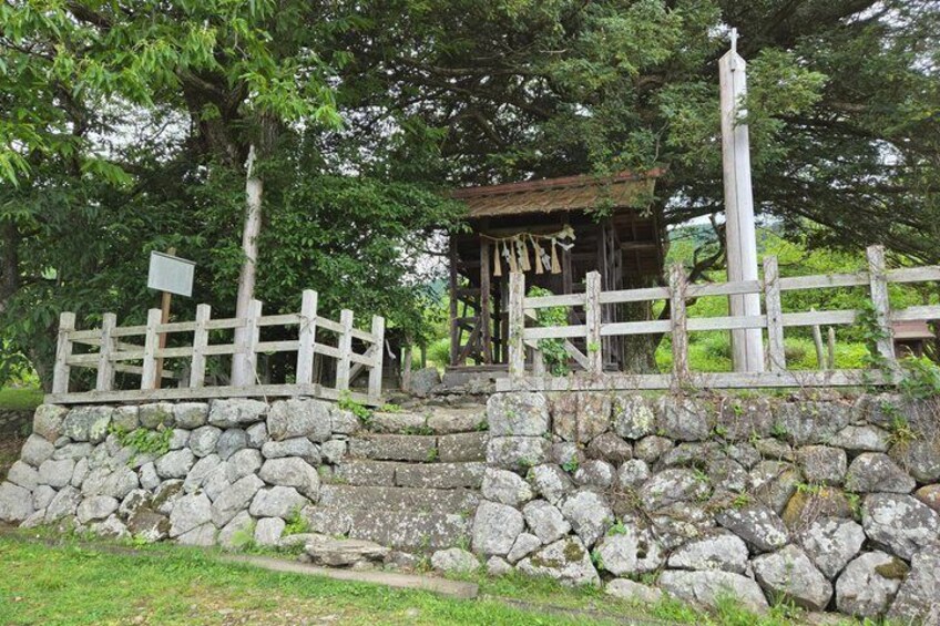 A stone wall, wooden fence, and a small shrine with a sign. 5