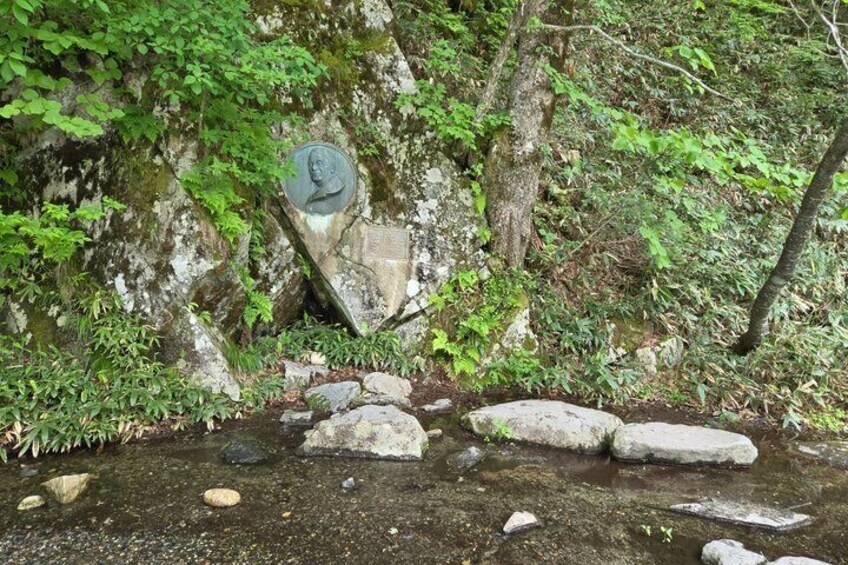 A natural setting with a stone monument, a stream, and surrounding greenery. 3