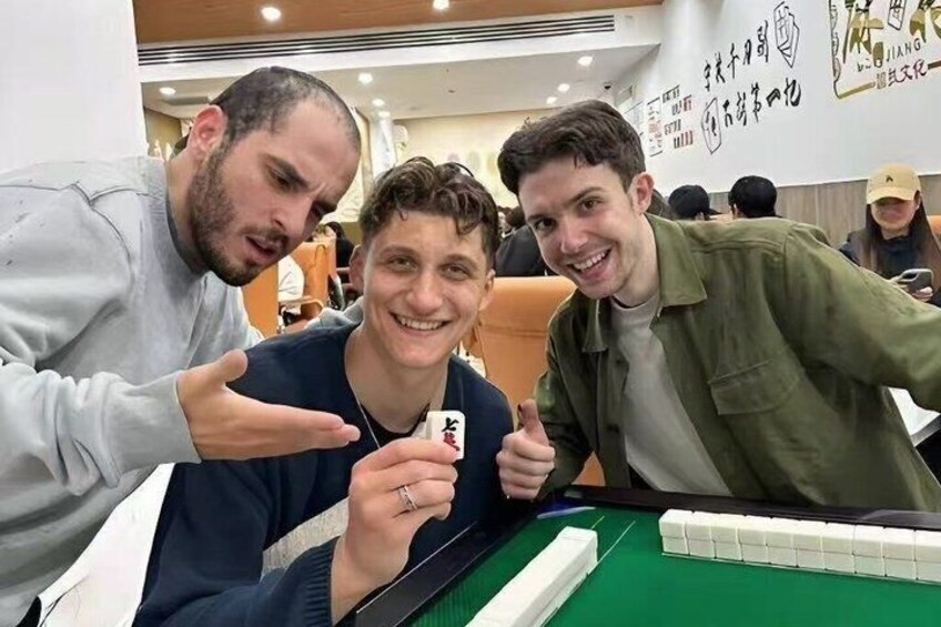 Three people at a pool table with a green felt surface, surrounded by a room with orange seating and walls with text. 2