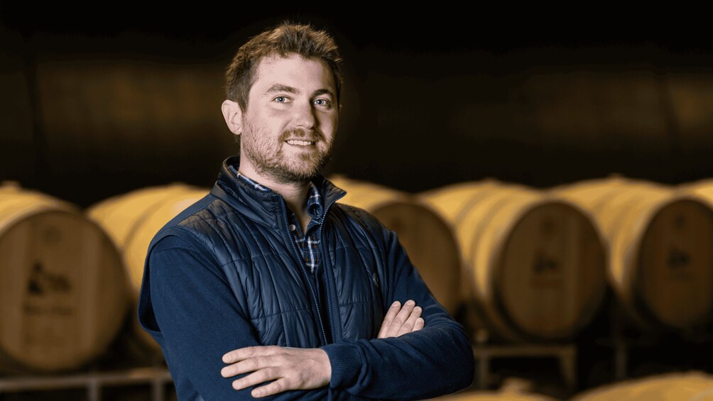 A person standing with arms crossed in front of barrels. 4