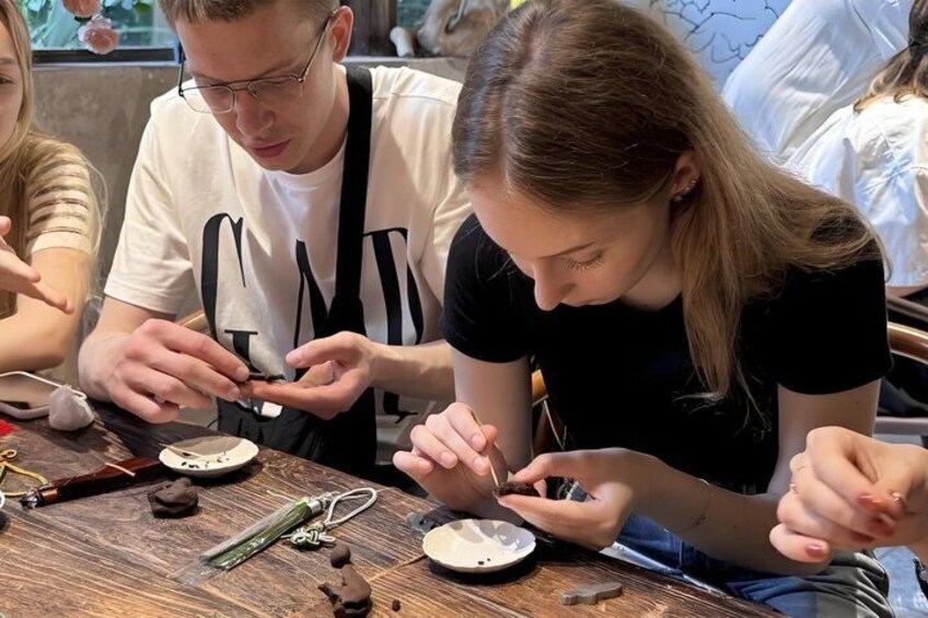 People engaged in a craft activity, possibly jewelry making, with tools and materials on a wooden table. 1