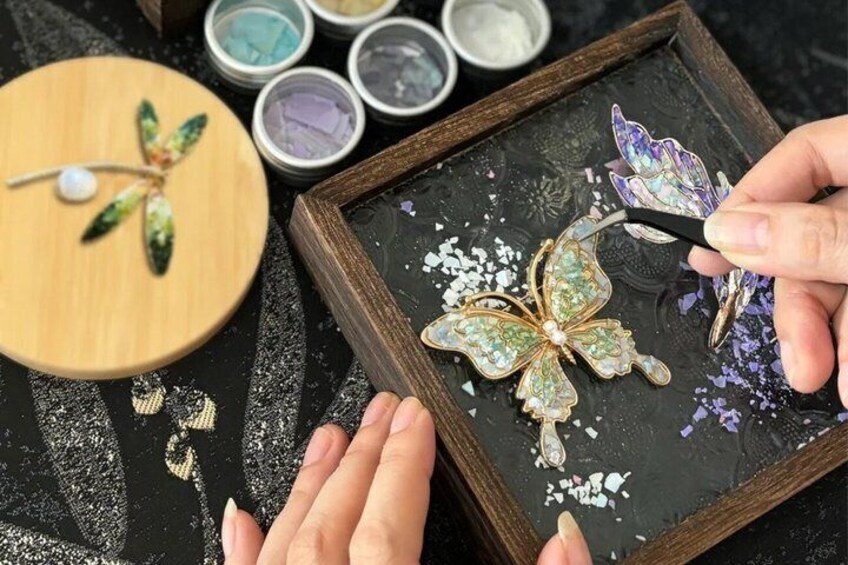 A person crafting a butterfly pendant with a pearl and colorful stones. 1