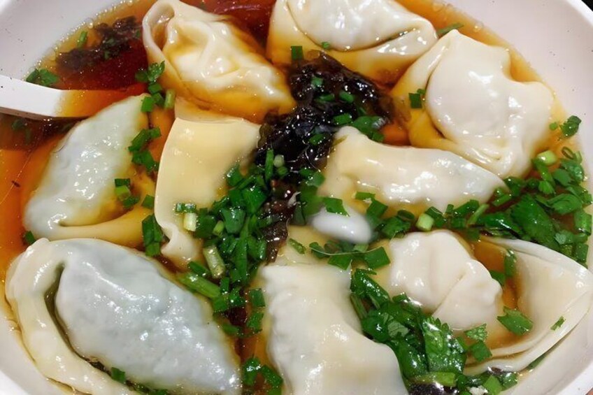 A bowl of dumplings in soup garnished with chopped green onions. 1