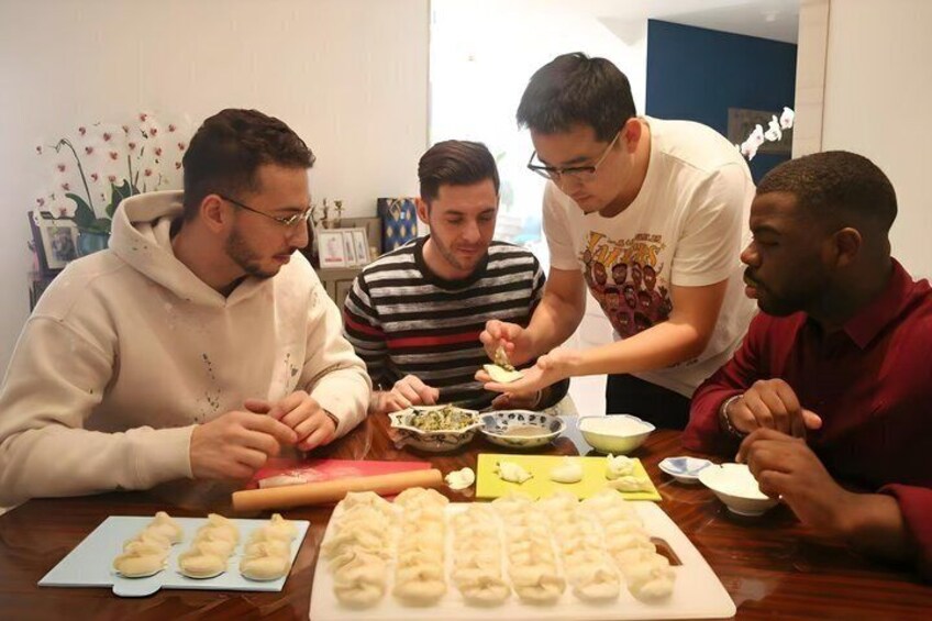 Four people preparing dumplings at a table with a variety of ingredients and tools. 1