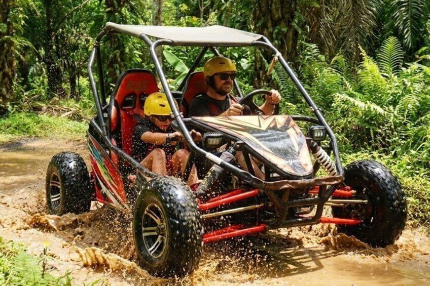 A red off-road vehicle driving through a muddy path in a forested area. 4
