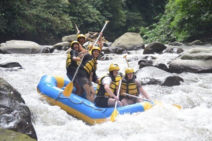 A group of people rafting on a blue raft in a river with rocks and greenery. 5