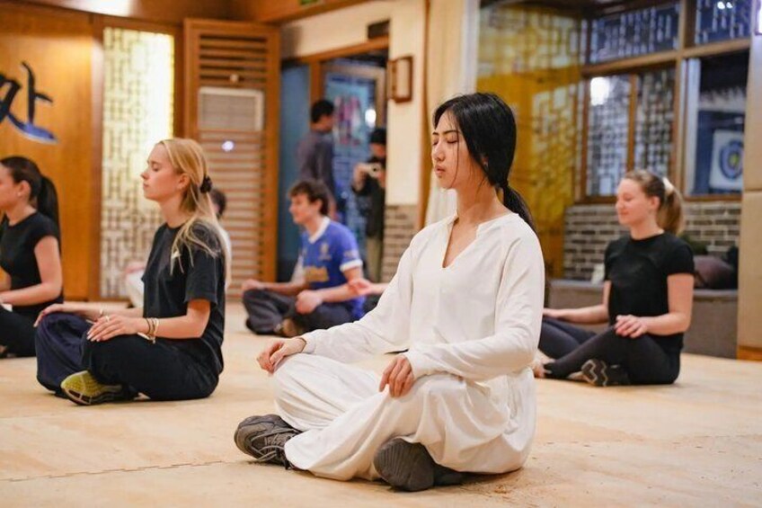 A group of people sitting cross-legged in a room with wooden walls and a patterned floor. 1