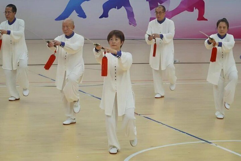 A group of people in white performing a synchronized dance with red tassels on a gymnasium floor. 2