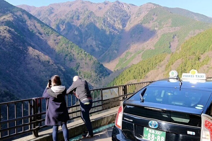 A black taxi with a 'YAKETAI' sign parked by a scenic mountain overlook. 3
