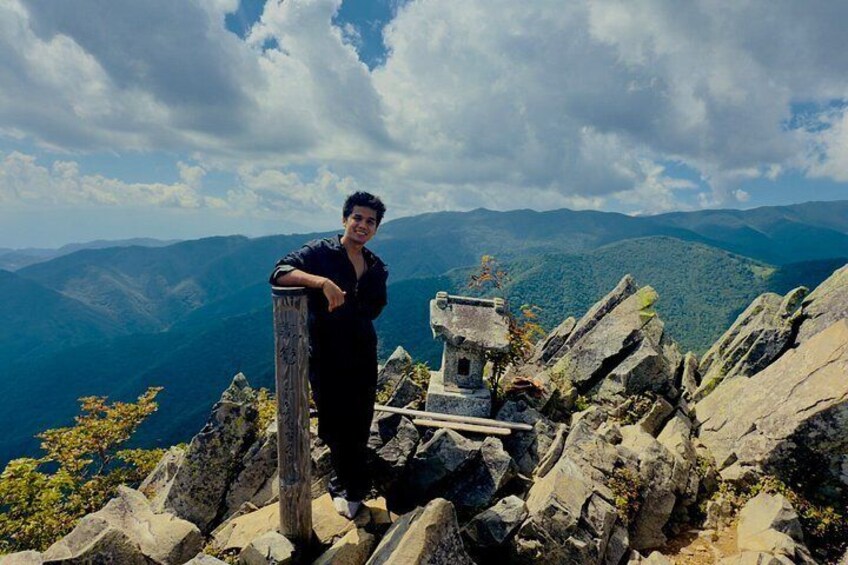 A person standing on a rocky mountain peak with a wooden structure and a scenic view of the mountains in the background. 4