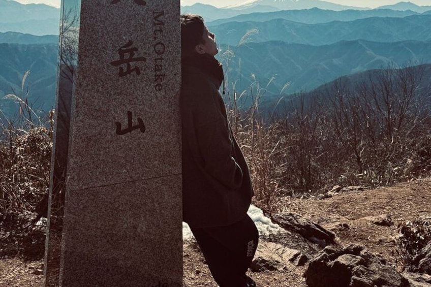 A person standing next to a stone monument with inscriptions, overlooking a mountainous landscape. 3