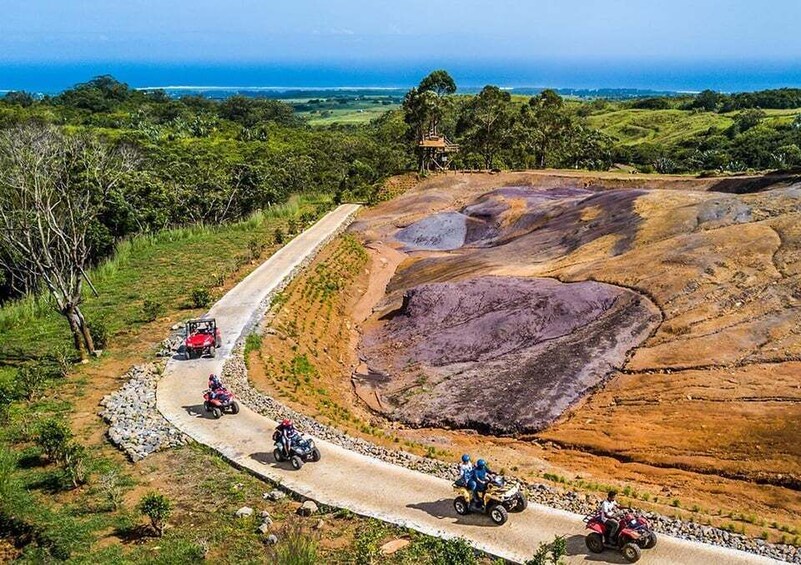 A dirt road with off-road vehicles, a rocky terrain, and a view of the ocean. 2