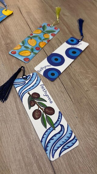 Three bookmarks with different designs and tassels on a wooden surface. 3
