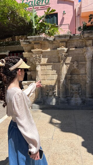 A person pointing at a stone structure with carvings, in front of a building with a cafe sign. 1