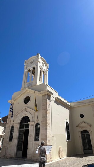 A church with a bell tower, a flag, and a person reading a sign. 2