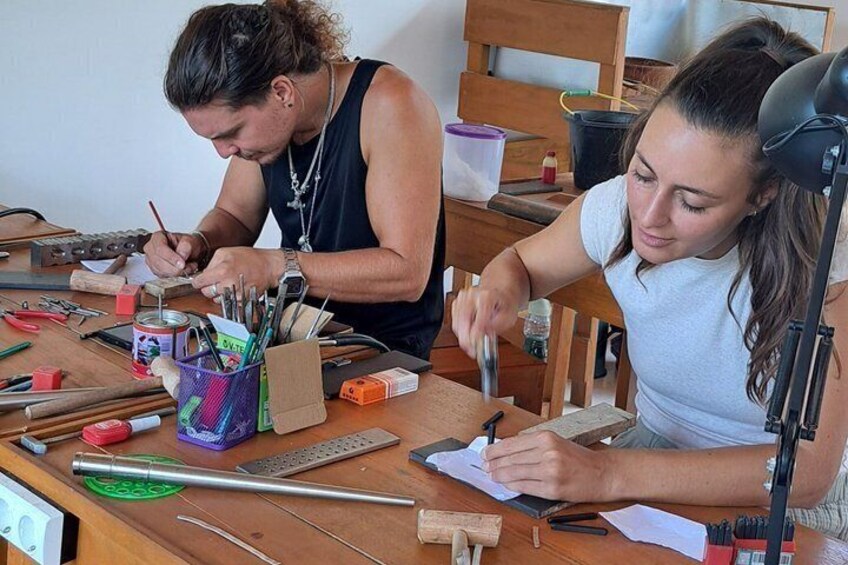 Dos personas trabajando en una mesa de madera con herramientas y materiales, probablemente dedicadas a una actividad artesanal o de reparación. 1