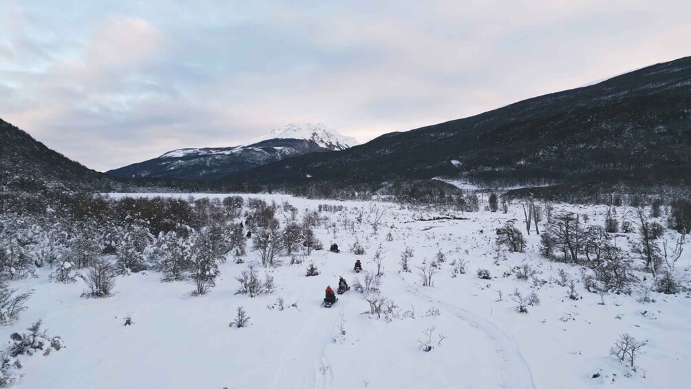 A snowy landscape with a clear sky, a mountain range in the background, and a person snowmobiling in the foreground. 5