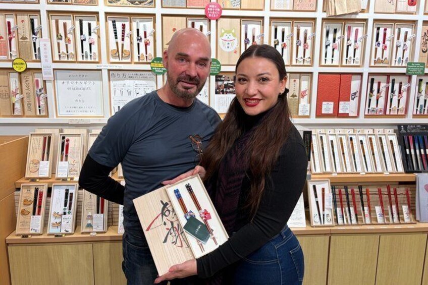Two people in a stationery store with shelves of pens and notebooks. 1