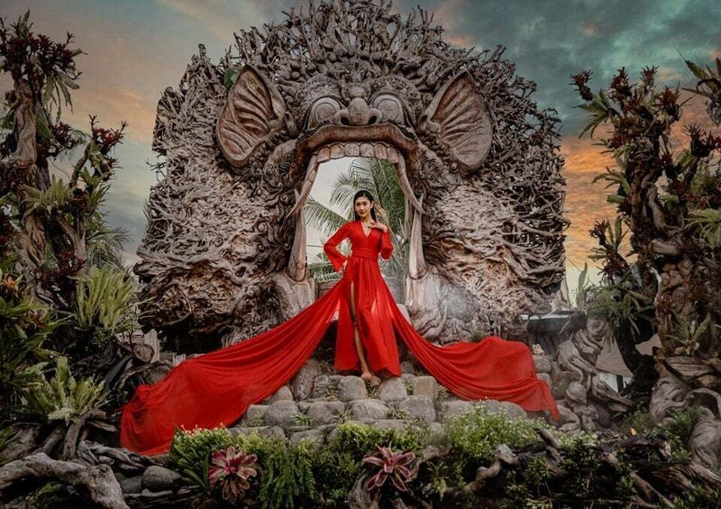A person in a red dress standing in front of a large, ornate stone structure with intricate carvings. 1