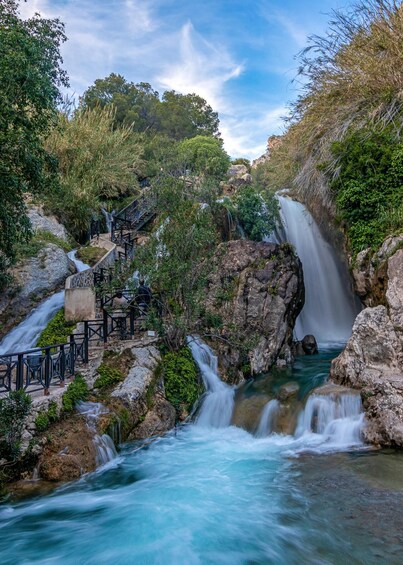 A waterfall cascading over rocks, surrounded by lush greenery and a viewing platform. 1