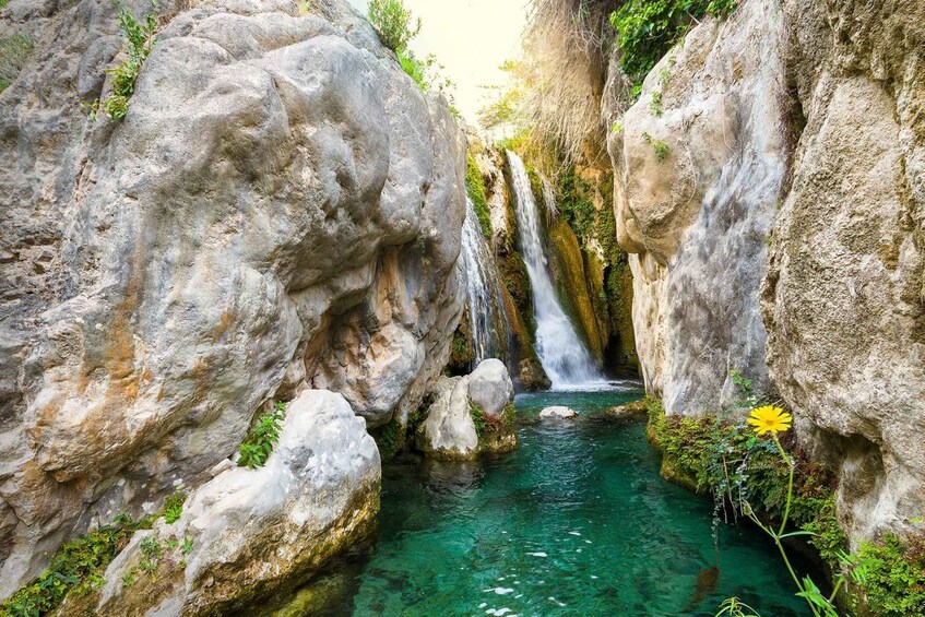A clear, turquoise stream flowing through a rocky gorge with a waterfall. 2