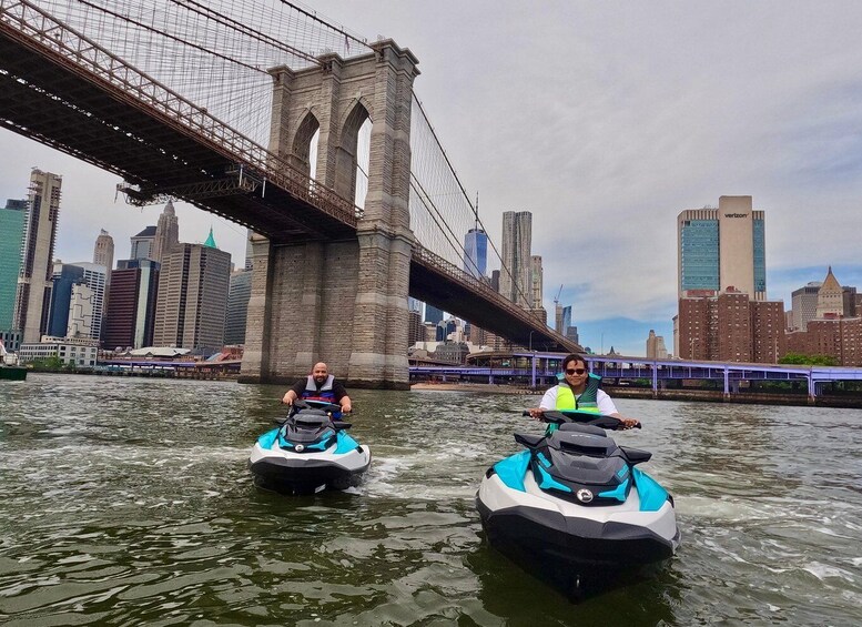 Two jet skis on a river with a city skyline and a bridge in the background. 1
