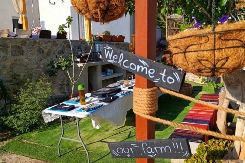A rustic outdoor setting with a welcome sign, a table with items on display, and a rope barrier. 5