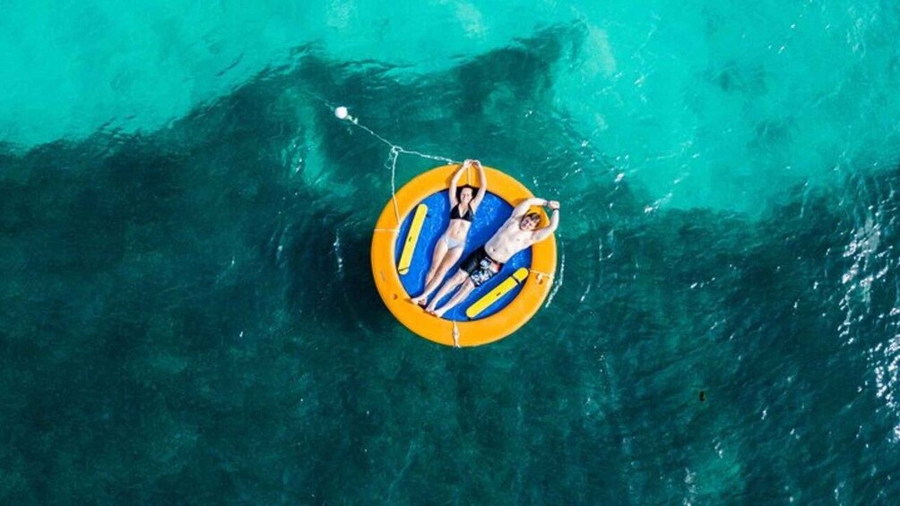 A person floating on a yellow and blue inflatable raft in turquoise water. 2