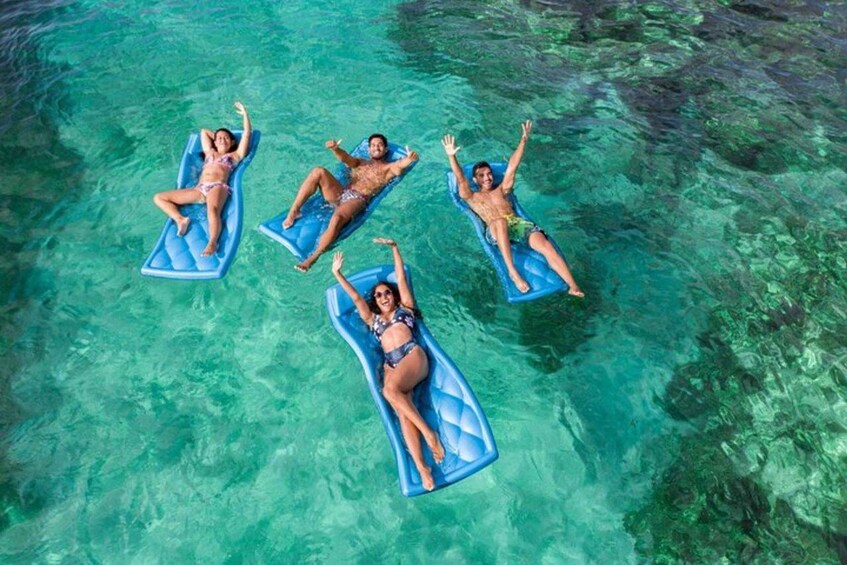 Four people floating on blue inflatable boards in clear turquoise water. 5