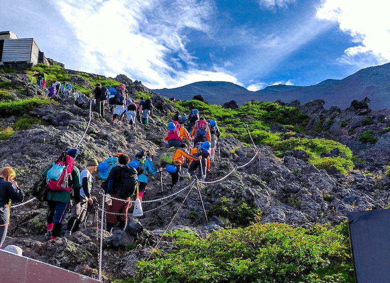 A group of hikers ascending a rocky mountain trail with a clear sky above. 1