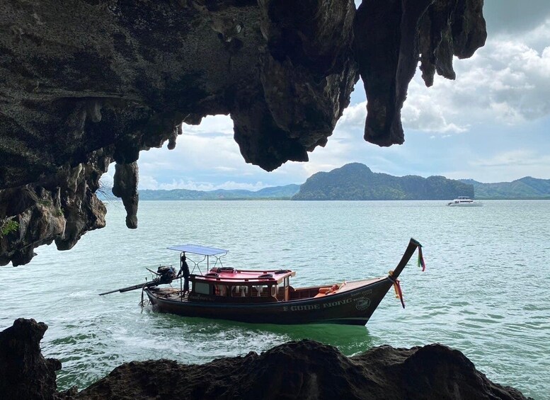 A boat named 'F GUIDE NONG' anchored near a cave entrance with a calm sea and distant mountains. 3