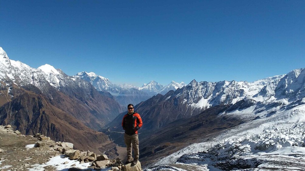 A person standing on a rocky mountain ridge with snow-covered peaks in the background. 3