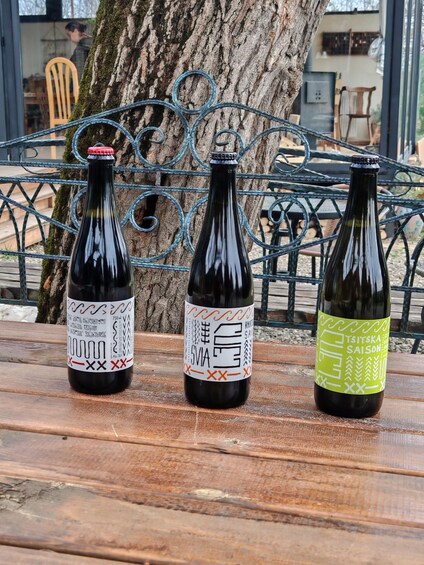 Three bottles of wine on a wooden table with a metal fence and a tree in the background. 3
