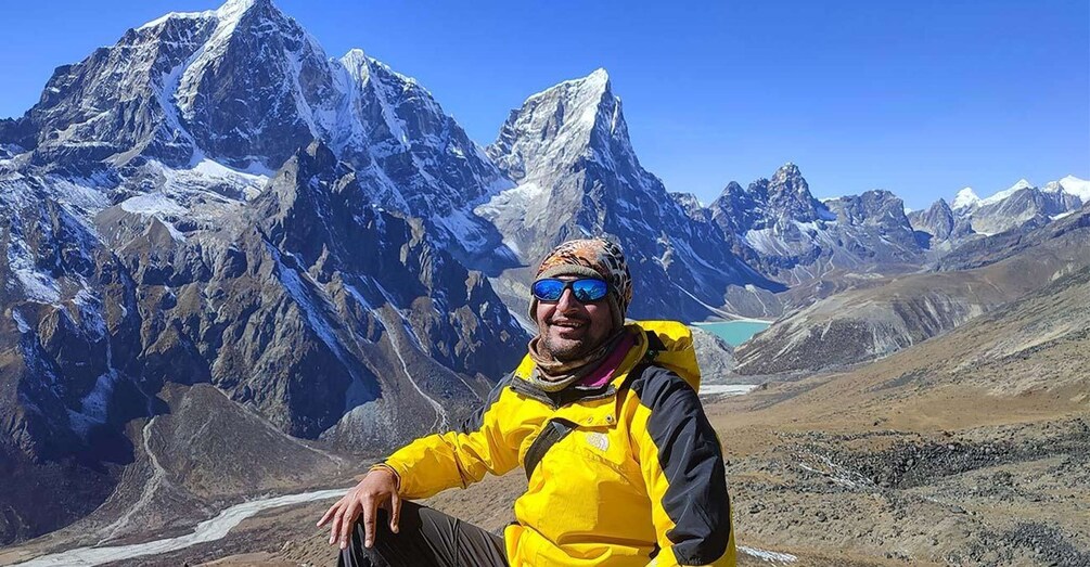 A person in a yellow jacket sitting on a mountain ridge with snow-capped peaks in the background. 3