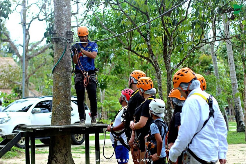 A group of people preparing for a zip-lining activity, with a guide standing on a platform. 4