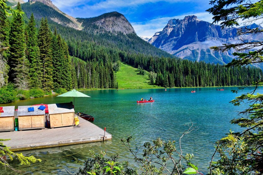 A lake surrounded by mountains, a dock with boats, and people kayaking. 2