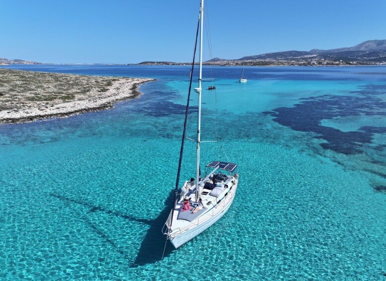 A sailboat anchored in clear turquoise waters with a rocky coastline and distant mountains. 5