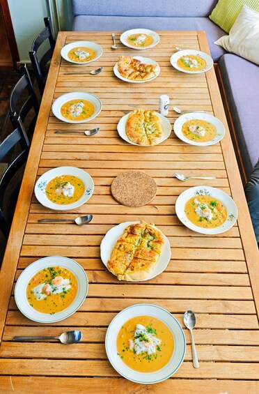 A wooden table with multiple bowls of soup and slices of bread, set on a wooden floor. 4
