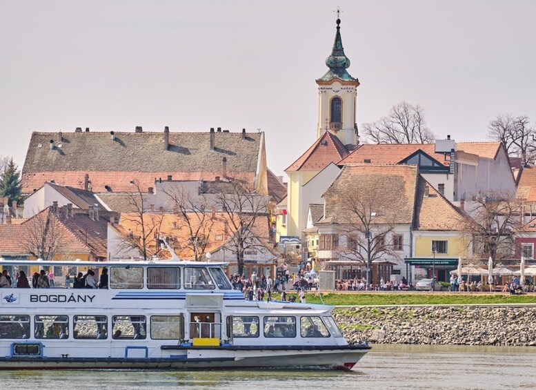 A boat named 'BOGDÁNY' on a river, with a church and buildings in the background. 5