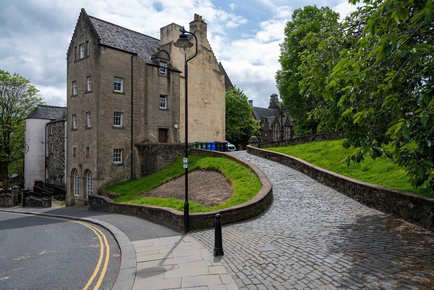 A historic stone building with a cobblestone pathway and lush greenery. 2