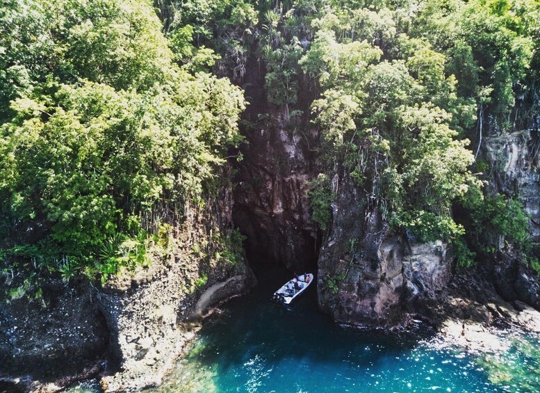 An aerial view of a coastal area with a boat near a rocky cliff and clear blue waters. 1