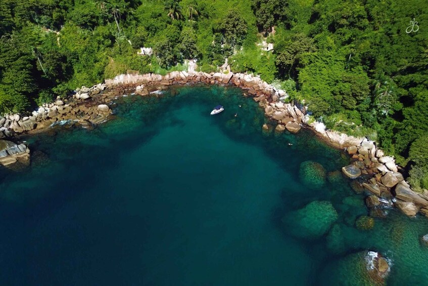 An aerial view of a coastal area with clear turquoise water, a rocky shoreline, and dense green vegetation. 2