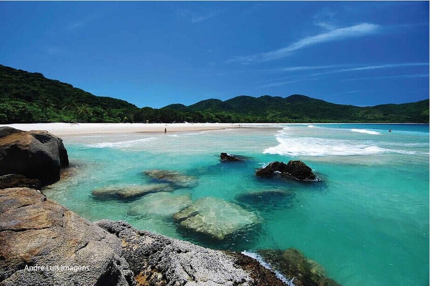 A beach with clear turquoise water, large rocks, and a forested hillside. 3