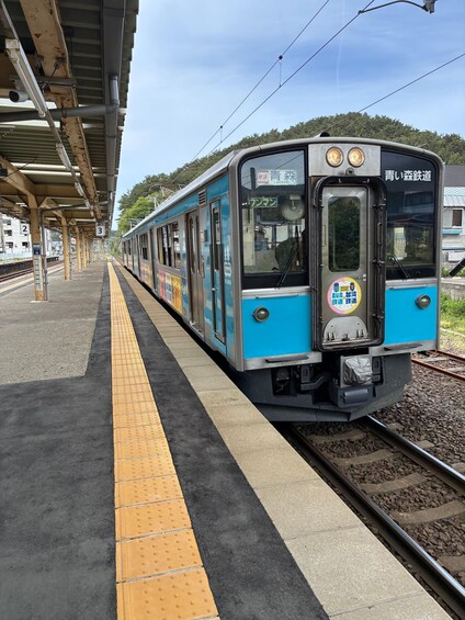 A blue train at a station platform with a yellow tactile paving strip. 1
