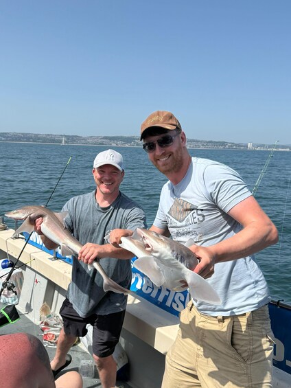 Two people holding a fish on a boat with a bridge in the background. 2