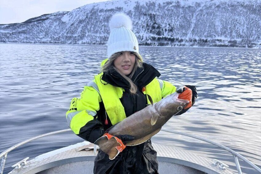 A person holding a fish on a boat with snow-covered hills in the background. 4