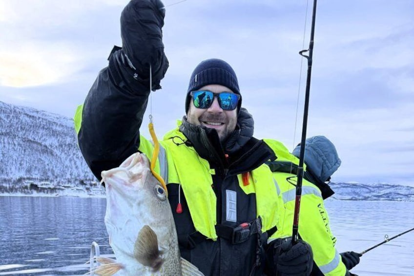 A person in a yellow jacket holding a fish and a fishing rod on a boat. 2